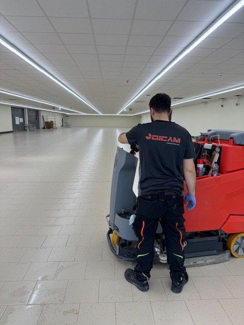 DICAM-Mitarbeiter reinigt mit einer Scheuersaugmaschine den Boden einer großen Halle
