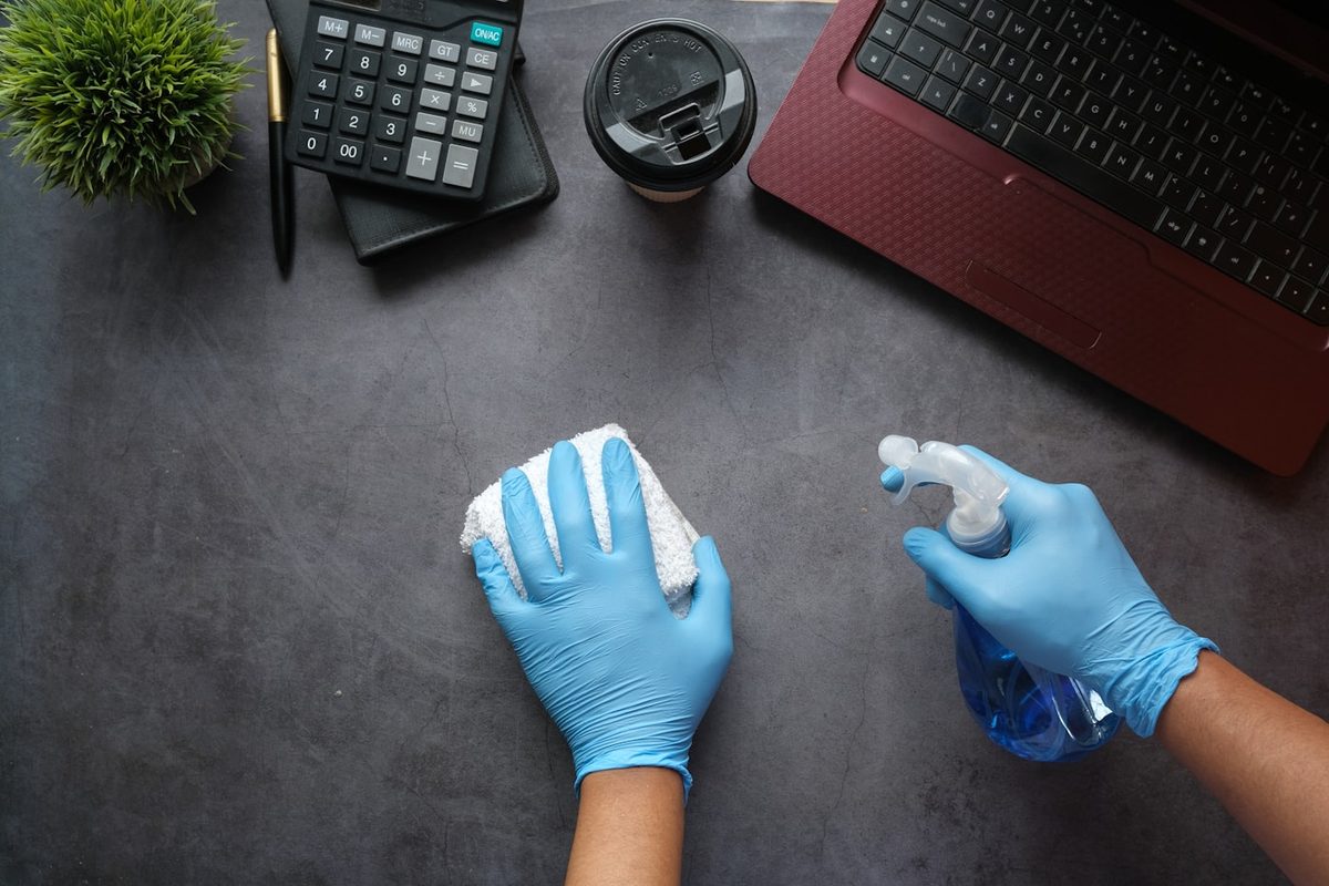 Reinigungskraft mit Handschuhen reinigt eine Schreibtischoberfläche