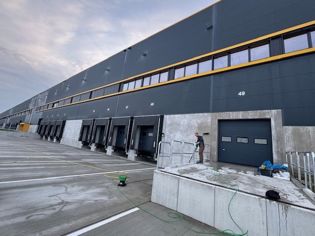 DICAM-Mitarbeiter reinigt die Fassade einer Logistikhalle an der Laderampe